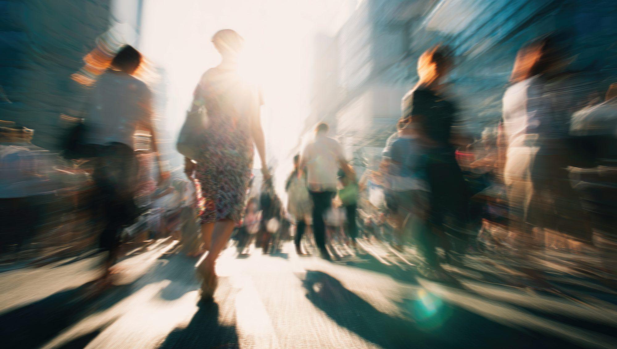 People moving through a sunlit city street, captured with motion blur.