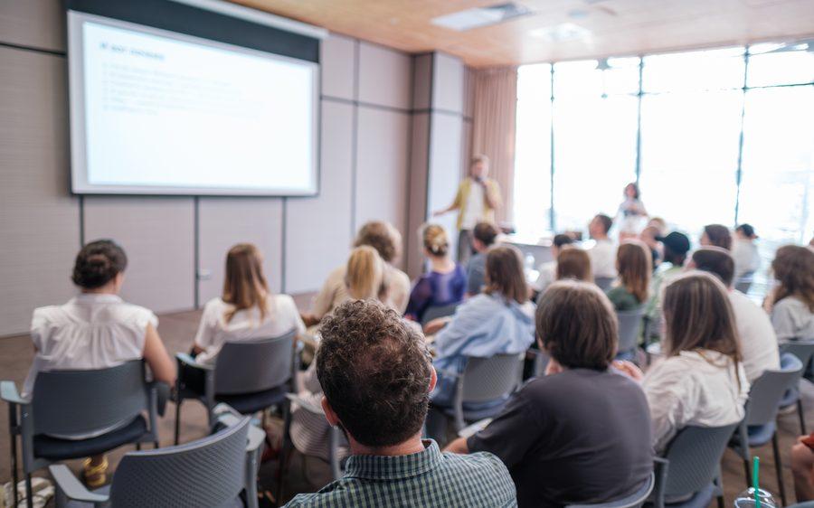 An audience seated in a conference room watching a presentation.