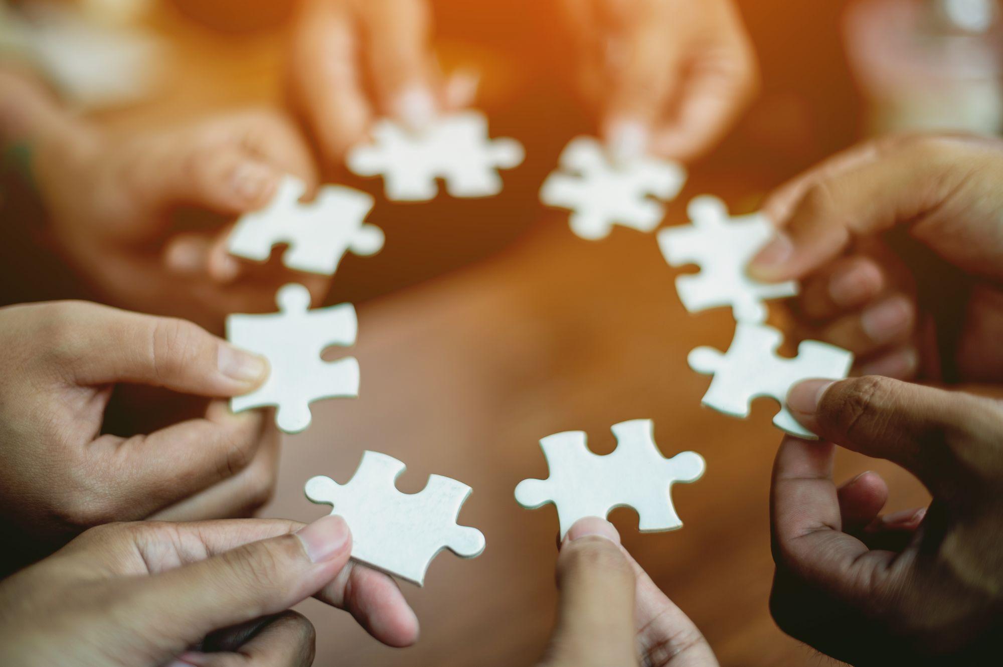 Hands holding white puzzle pieces forming a circle, symbolizing collaboration.